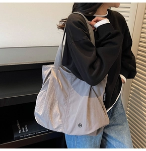 Detail of light gray nylon tote bag with CHUANGNI woven label and metal logo emblem