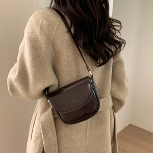 Close-up of a dark brown polished leather saddle bag worn over a beige wool coat