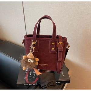Detail of burgundy leather bucket bag with gold lettering and brown monster plush charm