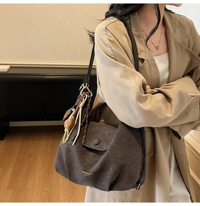 Détail du sac à bandoulière en cuir mat marron foncé avec pompon et breloque peluche