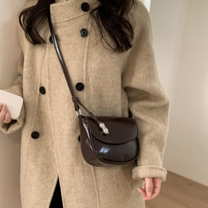 Close-up of brown wax leather saddle bag with silver peanut charm and fine strap