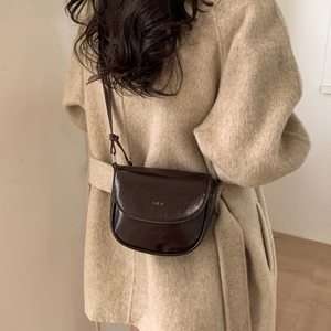 Detail of a dark brown half-moon saddle bag with adjustable strap on a wool coat