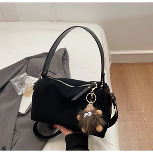 Detail of black suede Boston bag featuring a plush monster charm and leather strap