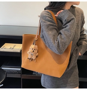 Braune Shopper-Tasche aus Leder am Modell mit süßem Teddybär-Anhänger als Detail