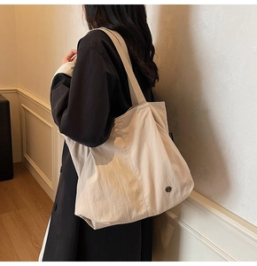 Detailed close-up of light beige tote bag texture and brand tag on nylon shoulder bag