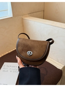 Close-up of brown suede saddle bag featuring a round metal twist lock and leather trim