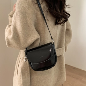 Detail of a black glossy saddle bag with a silver peanut pendant on a beige wool coat