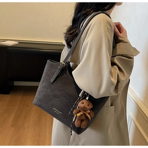 Détail d'un sac cabas en daim gris foncé avec bandoulière et breloque ours
