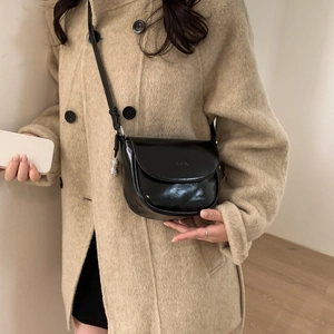 Polished black PU leather saddle bag with silver peanut charm on beige coat