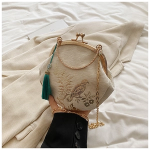 Detail of embroidered floral shell bag with golden metal frame and green tassel charm
