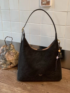 Retro black suede hobo bag with gold logo and vintage wood bead charm on wooden desk
