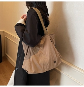 Detail view of khaki nylon tote bag with wide shoulder strap worn by model in minimalist setting
