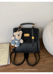 Detail of vintage black leather backpack featuring a suede panel and cute bear charm