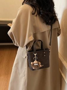 Brown mini bucket bag with plush charm and fashion logo shown on model with trench coat