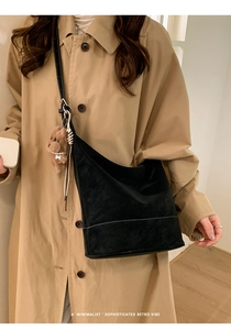 Detail of black suede bucket bag with white stitching and a cute bear keychain
