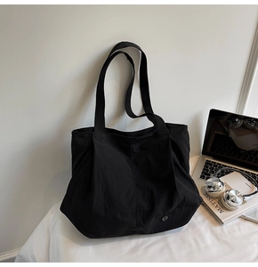 Detail of black tote bag featuring a circular metal logo and pleated bottom design