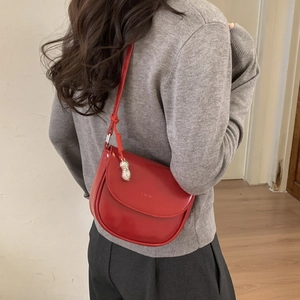 Detail of red saddle bag with knot strap and silver peanut pendant shown on model
