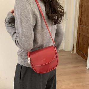 Detail of red saddle bag with embossed logo and unique silver peanut metal charm pendant