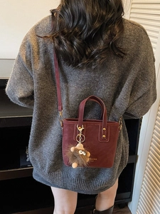 Fashionable burgundy bucket bag with plush monster charm and adjustable strap
