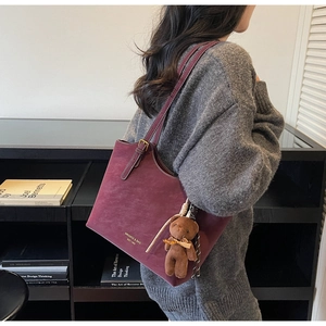 Détail d'un sac cabas bordeaux en suédine avec logo doré et charmant pendentif petit ours