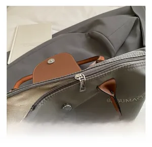 Gros plan sur la fermeture éclair et les garnitures en cuir de ce sac en nylon gris