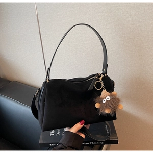 Detail of black suede hobo bag with leather strap and plush monster charm on sofa