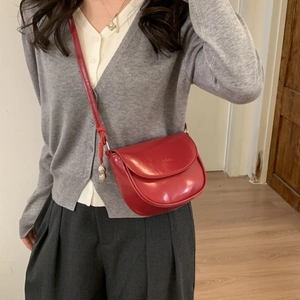 Detailed view of a red leather saddle bag featuring a unique golden peanut charm and strap