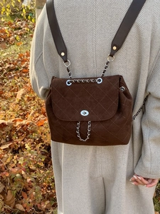 Quilted dark brown bucket backpack with silver turn-lock in autumn outdoor setting