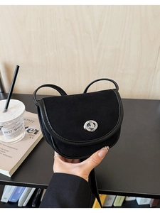 Detail of a black matte saddle bag featuring a silver circular clasp and mixed textures