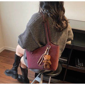 Détail du sac cabas bordeaux avec logo doré, breloque ours et pompon tressé