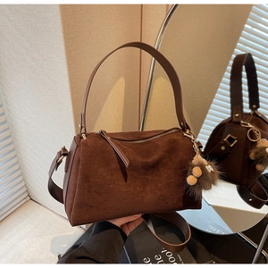 Detail of dark brown suede pillow bag with plush charm and elegant metallic zipper