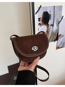 Detail of dark brown saddle bag with matte suede texture and silver round metal lock
