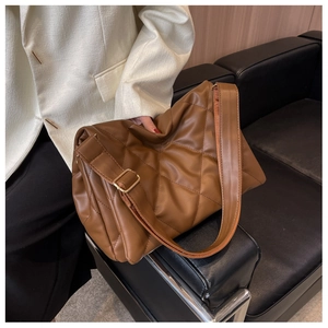 Detail of caramel quilted shoulder bag with wide adjustable strap on a dark leather sofa