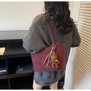 Détail du sac cabas bordeaux avec breloque ours porté par un mannequin en scène