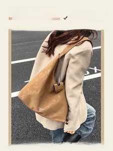 Gros plan d'un grand sac cabas en cuir mat marron porté avec un blazer beige chic