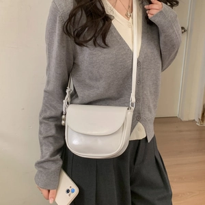 Detailed view of a white saddle bag with a minimalist flap and crossbody strap