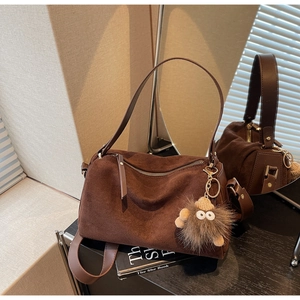 Detail of dark brown suede pillow bag featuring a cute plush monster charm and leather strap
