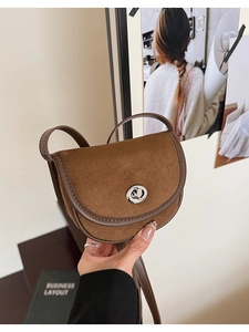Close-up of brown suede saddle bag with silver metallic twist lock and leather piping