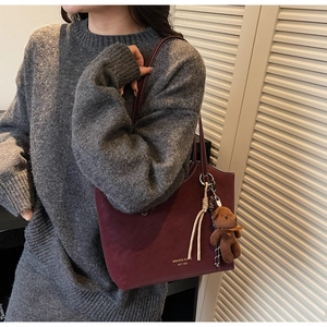 Détail du sac cabas bordeaux avec lettrage doré, breloque ours en peluche et gland