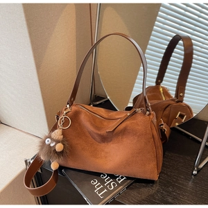 Close-up of brown frosted Boston bag with plush pompom and matching wide strap detail