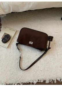Close-up of retro brown suede shoulder bag with metallic twist lock on a soft beige rug