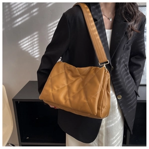 Detailed close-up of ginger yellow quilted faux leather crossbody bag with wide strap