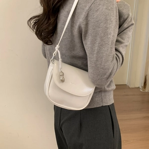 Detail of a creamy white saddle bag with a silver peanut charm on a grey sweater