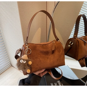 Detailed view of brown suede pillow bag featuring a plush monster charm and smooth strap