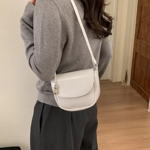 Detailed side view of a white leather saddle bag with silver charm on a model's shoulder