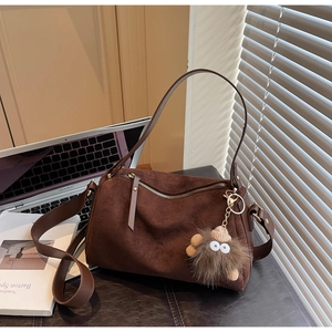 Detail of dark brown suede Boston bag with adjustable strap and plush monster pendant