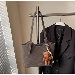 Détail du sac cabas en daim marron avec logo, breloque ours et ombres texturées