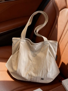 Minimalist beige nylon tote bag with shoulder straps on a leather car seat