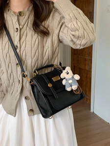 Retro black leather backpack with flap and cute bear pendant shown on model in warm interior