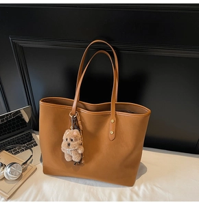 Große braune Shopper-Tasche mit süßem Plüsch-Hundeanhänger auf einem modernen Schreibtisch